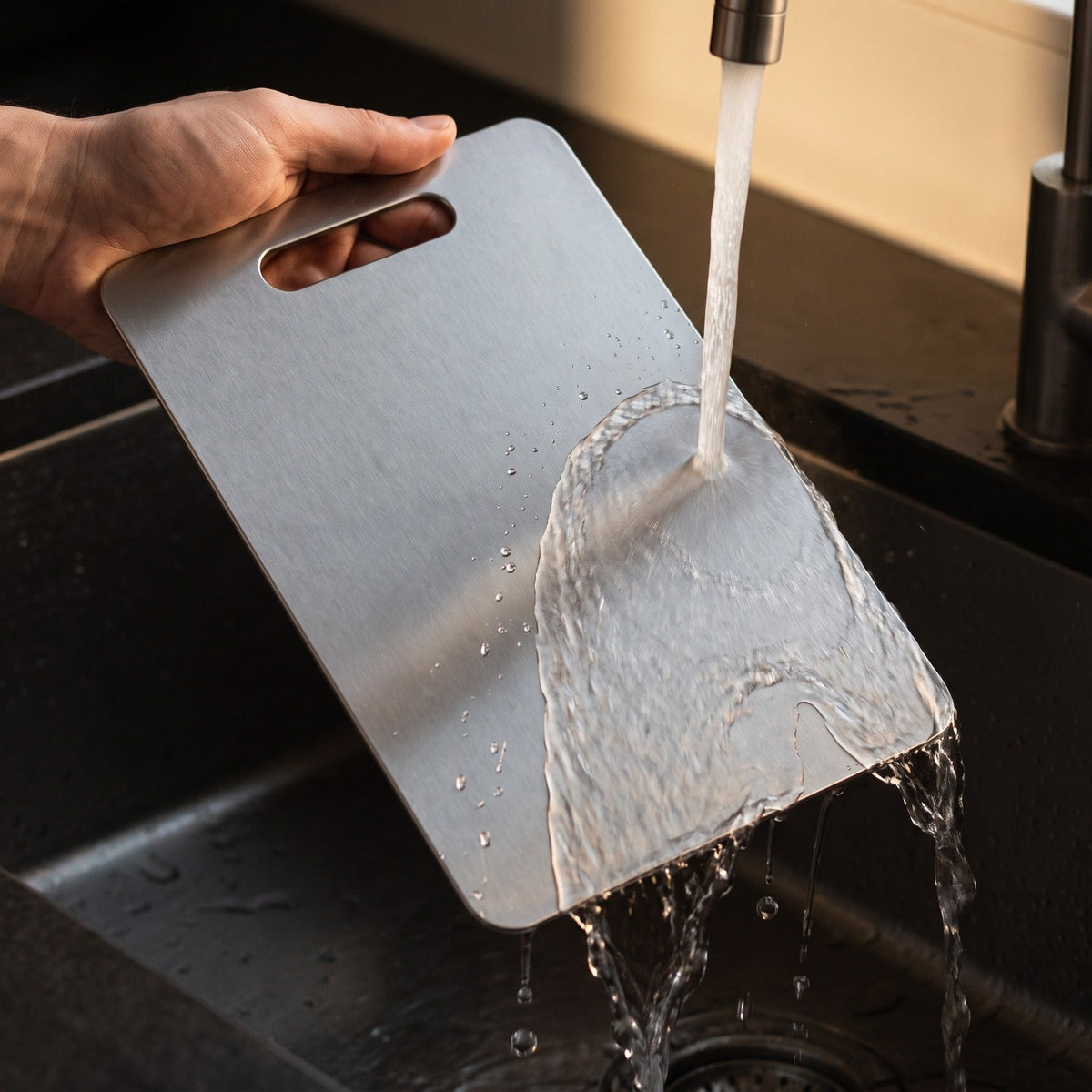 Titanium cutting board being rinsed under a running kitchen tap
