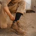Man pulling a black alpaca crew sock up over his work boot
