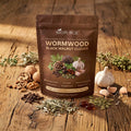 Pouch of wormwood and black walnut softgels on a wooden table with walnuts, garlic and herbs