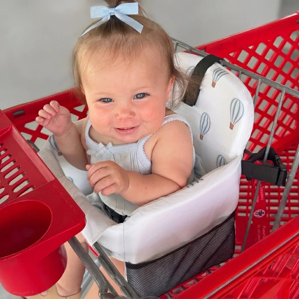 Smiling baby sitting in the padded seat inside a red shopping cart