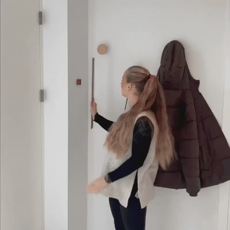 Woman taking the shoehorn off its wall mount next to a coat