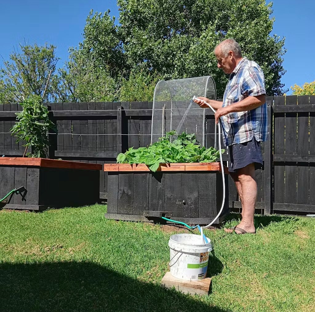 Man watering a garden bed with the pump in a bucket
