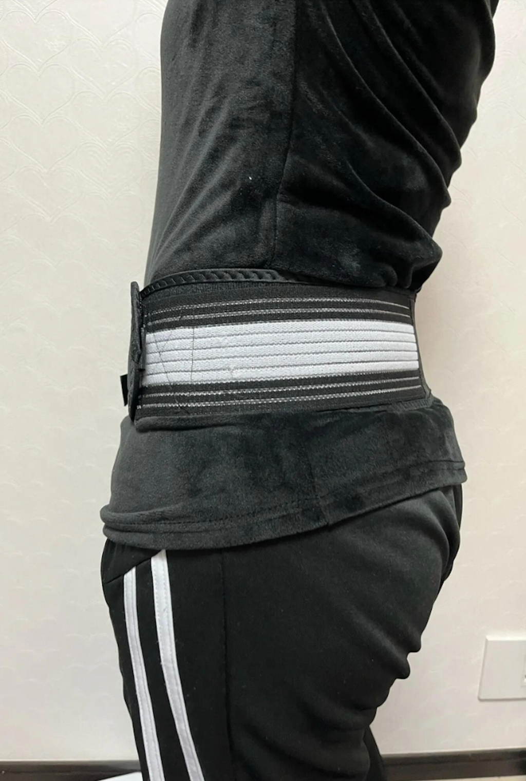 Hip belt with grey and white elastic straps worn around the hips over dark trousers