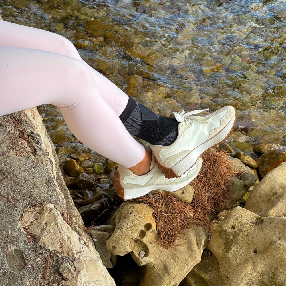Woman sitting on rocks wearing the foot sleeve with trainers