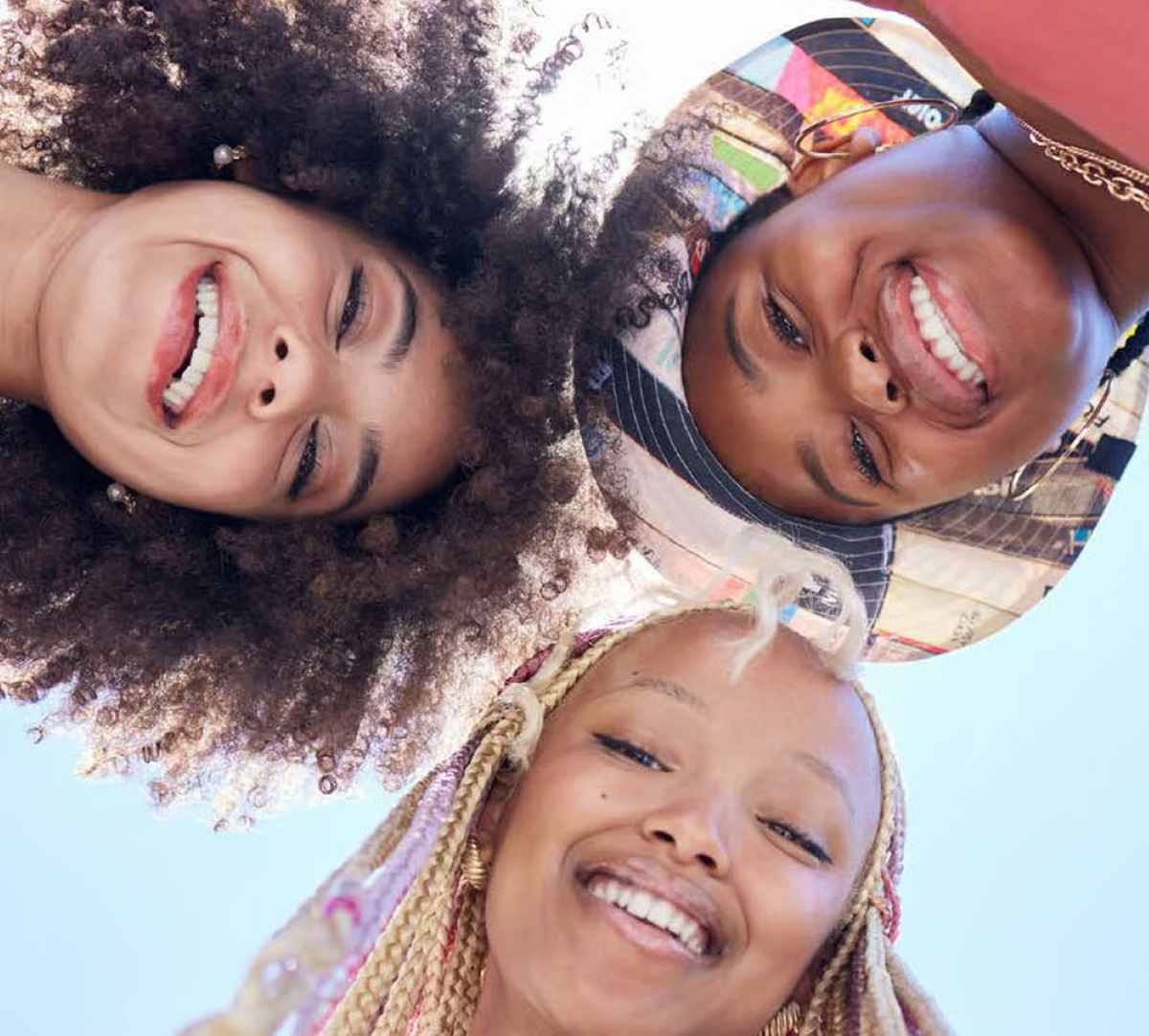 Three smiling friends seen from below against a blue sky
