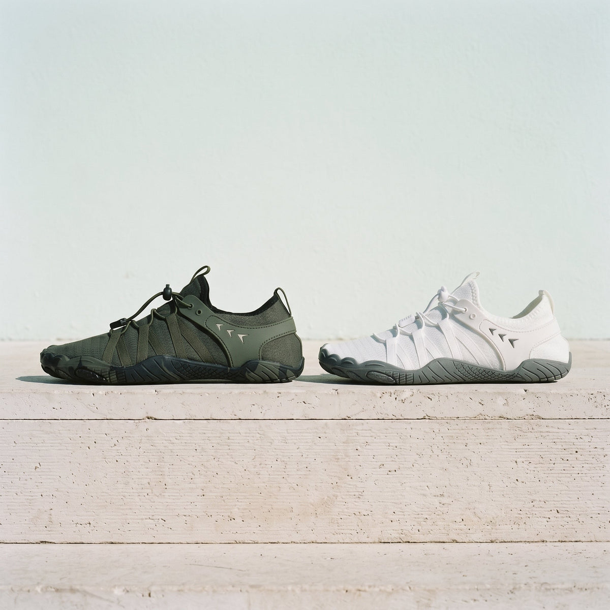 Green and white barefoot shoes side by side on a stone ledge