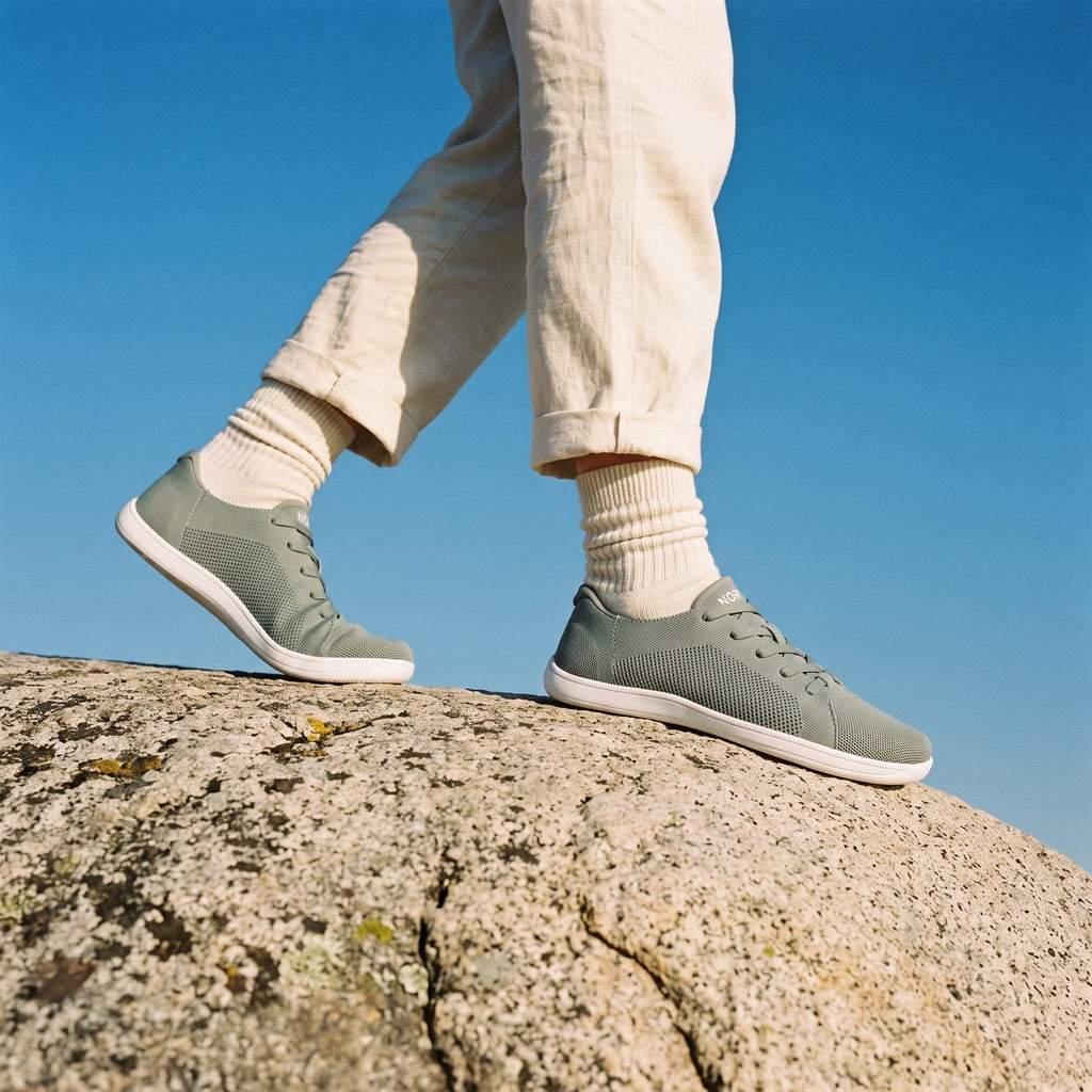 Person walking on a rock outdoors in sage green knit barefoot sneakers
