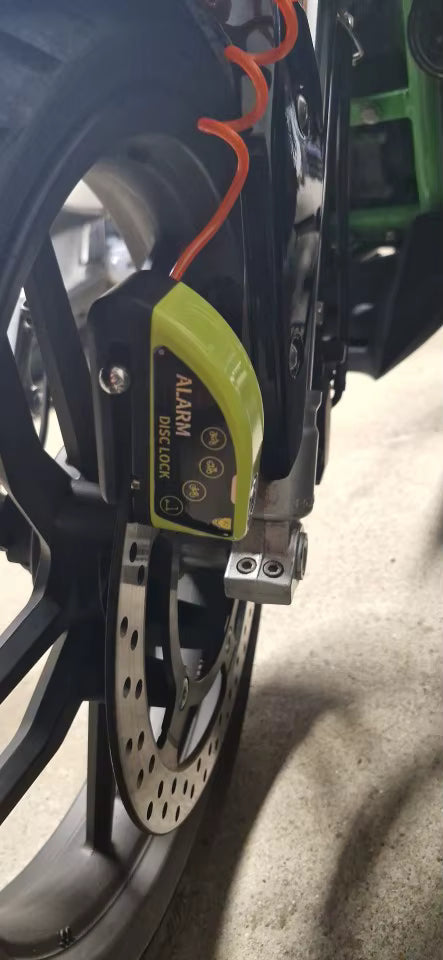Yellow alarm disc lock fitted to the front brake disc of a motorbike