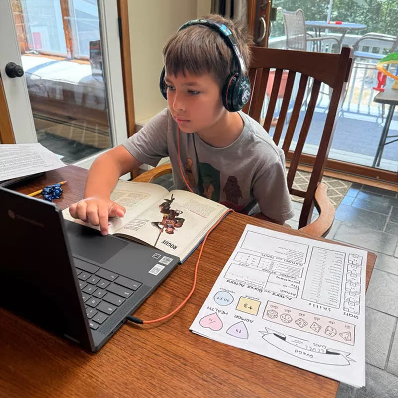Boy doing homework at a table with headphones and a laptop