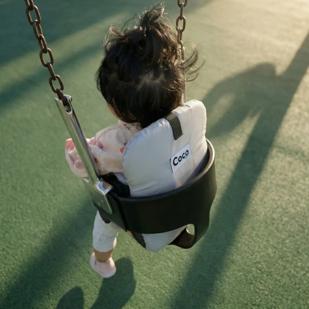 Toddler on a park swing sitting in the padded seat
