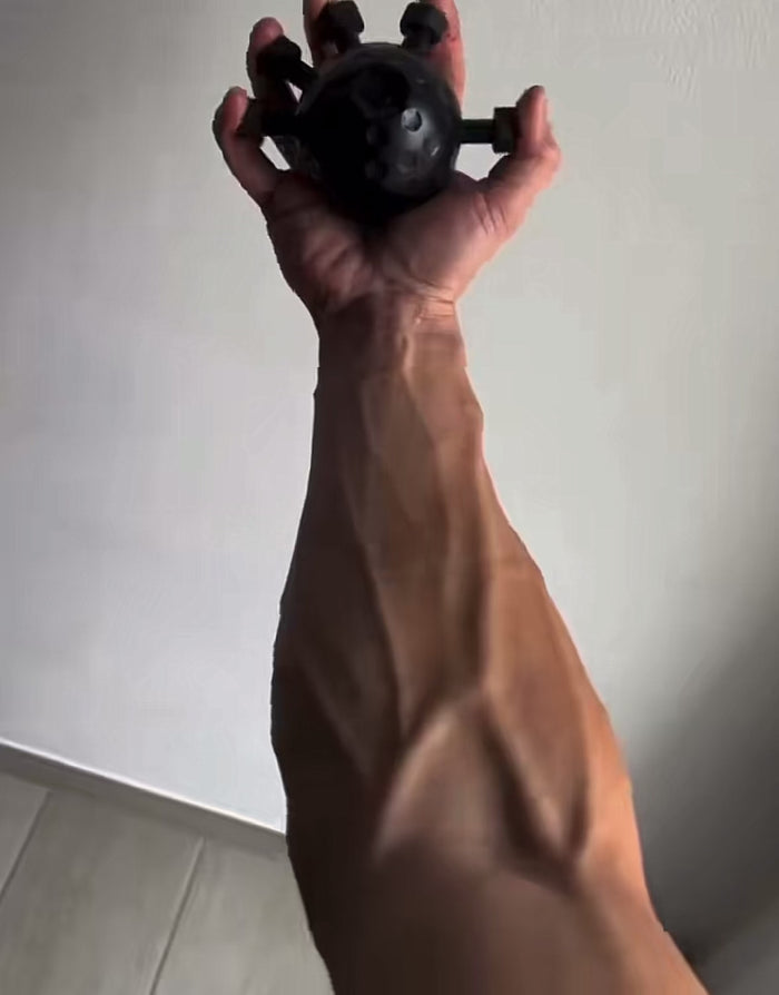 Hand squeezing a black forearm training ball with flexible finger pegs