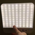 Ultra-thin square LED panel light glowing bright white, held in one hand