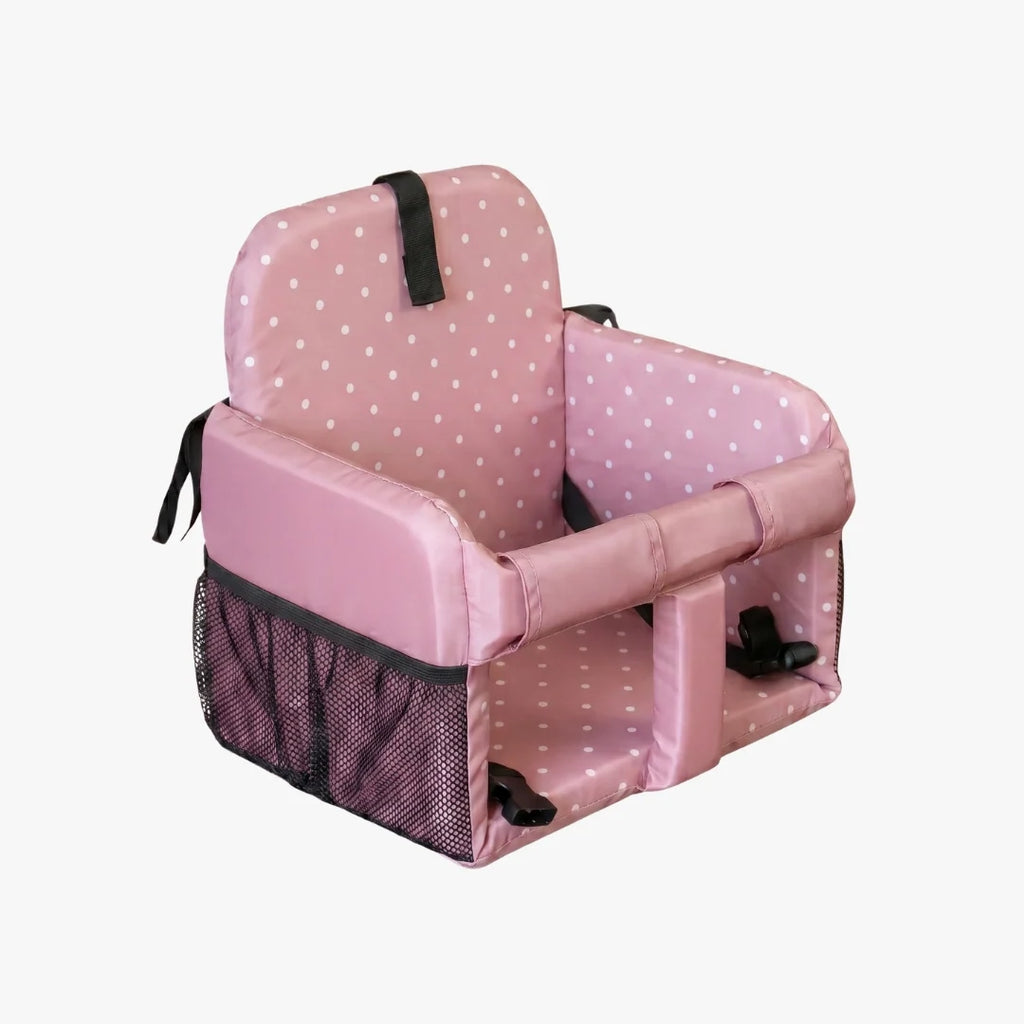 A pink padded child's booster seat with white polka dots, black mesh side pockets, and black safety straps, shown on a plain light gray background.