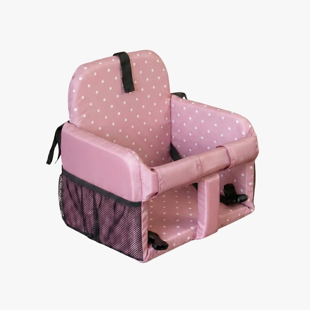 A pink padded child's booster seat with white polka dots, black mesh side pockets, and black safety straps, shown on a plain light gray background.