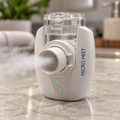 Small white handheld mesh nebulizer releasing a fine mist on a kitchen counter