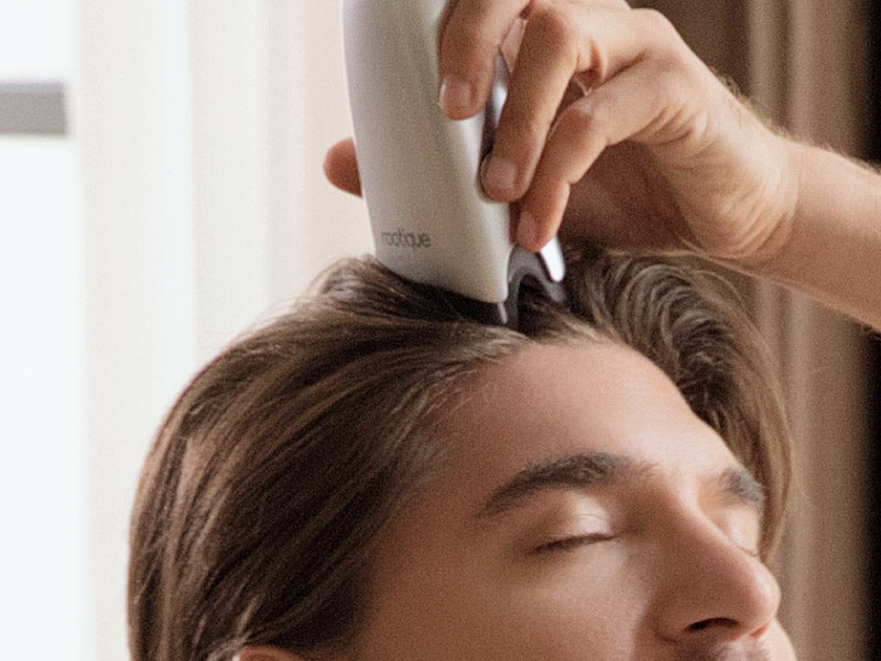 Man gliding the silver scalp applicator from his hairline back through his hair