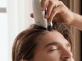 Man gliding the silver scalp applicator from his hairline back through his hair